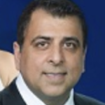 Headshot of man in a black suit with blue background