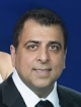 Headshot of man in a black suit with blue background