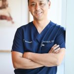 Doctor in blue scrubs standing leaning against a wall