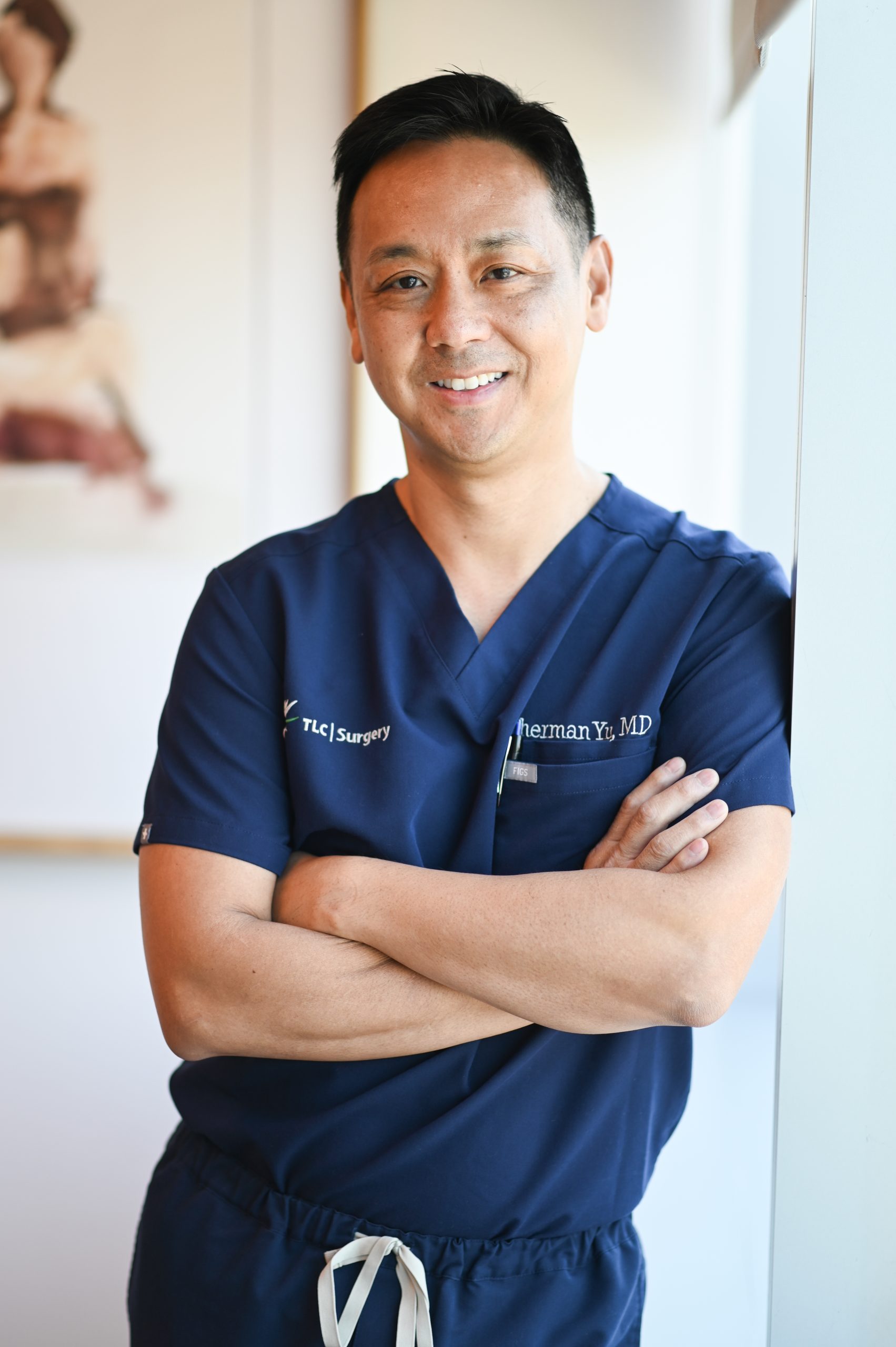 Doctor in blue scrubs standing leaning against a wall